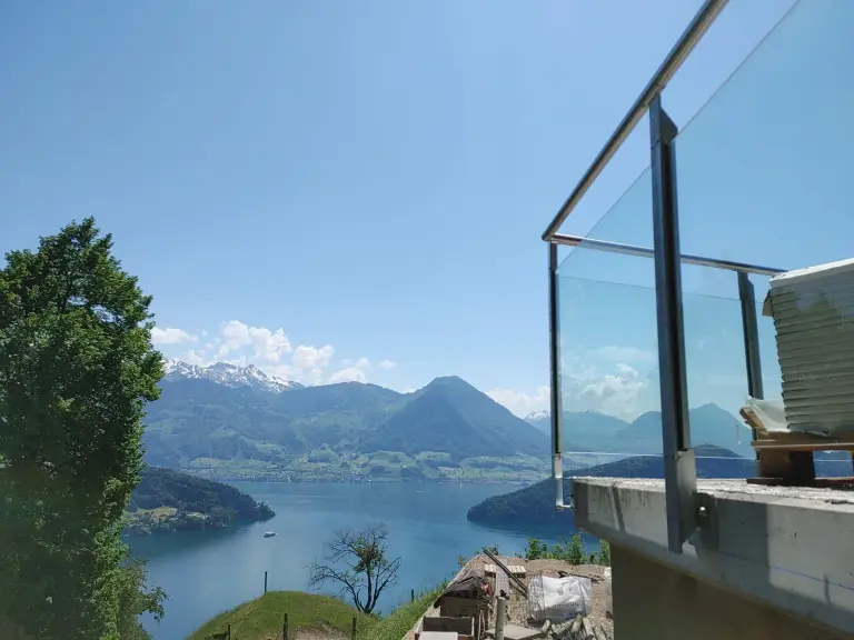Glasgeländer mit Klarglas, dahinter See und Berge